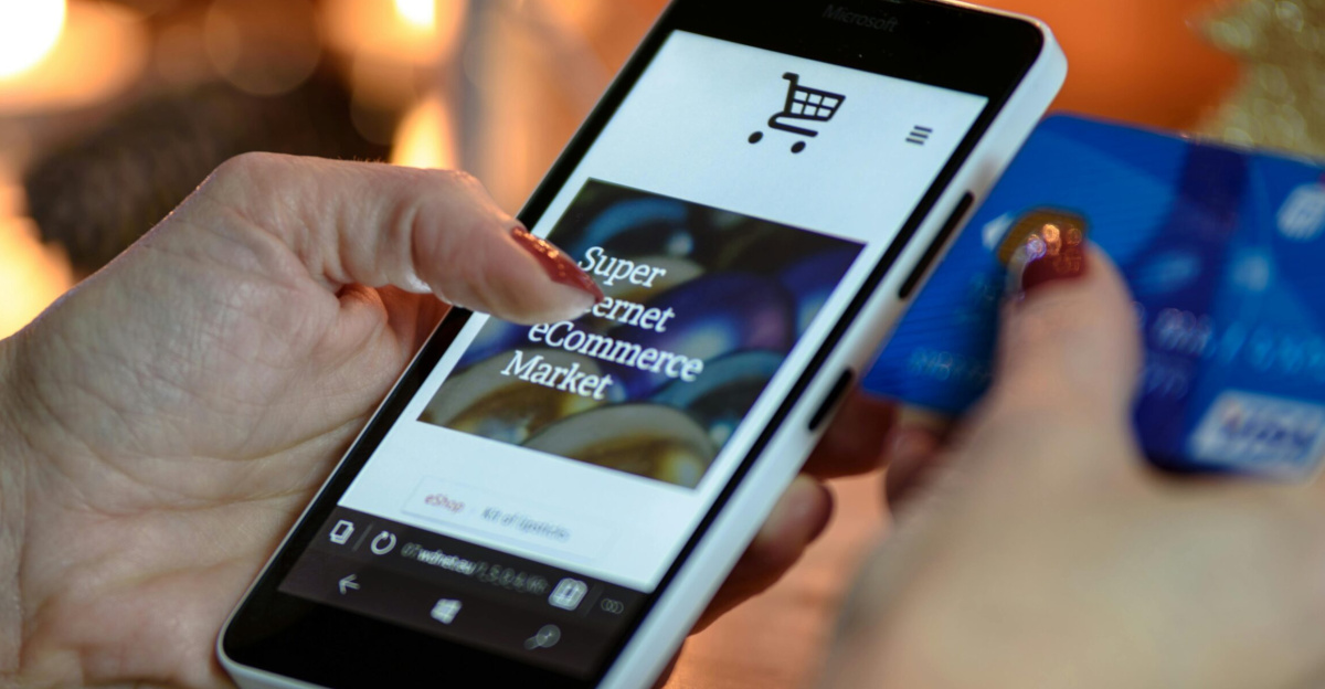 Woman using smartphone for online shopping with credit card in hand, festive background lighting.