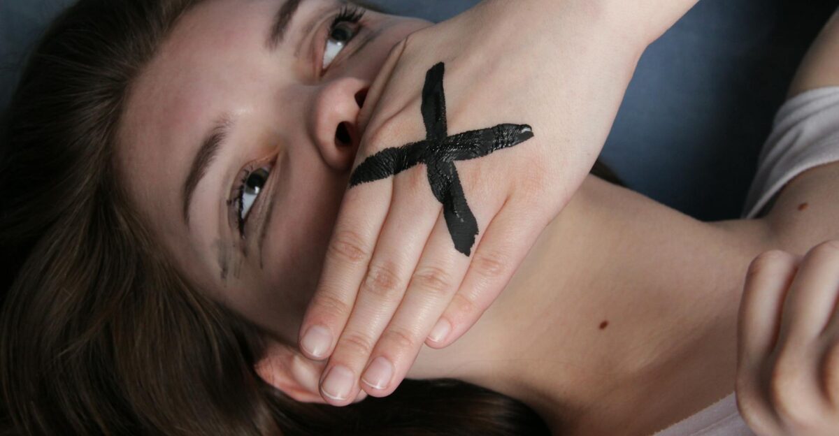 A conceptual portrait of a woman with a marked hand over her mouth symbolizing silence or censorship