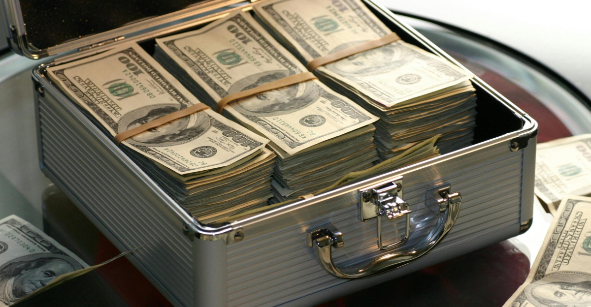 Open briefcase filled with stacks of hundred dollar bills on a glass table, representing wealth.