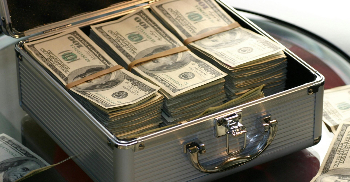 Open briefcase filled with stacks of hundred dollar bills on a glass table, representing wealth.