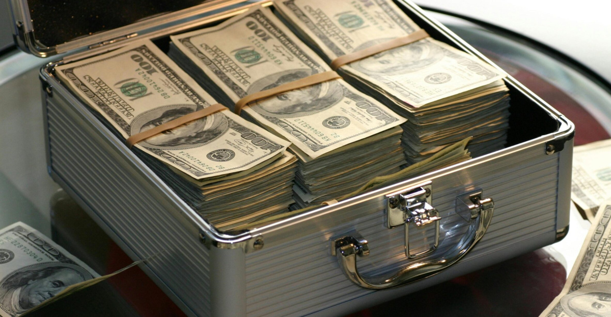 Open briefcase filled with stacks of hundred dollar bills on a glass table, representing wealth.