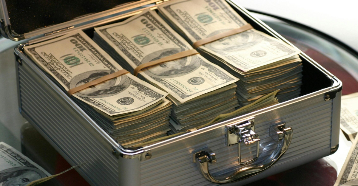 Open briefcase filled with stacks of hundred dollar bills on a glass table, representing wealth.