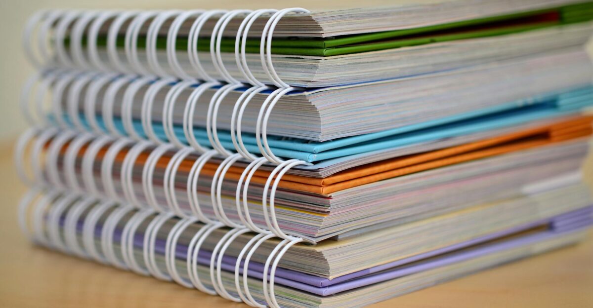 A colorful stack of spiral-bound notebooks neatly placed on a wooden desk Ideal for educational themes
