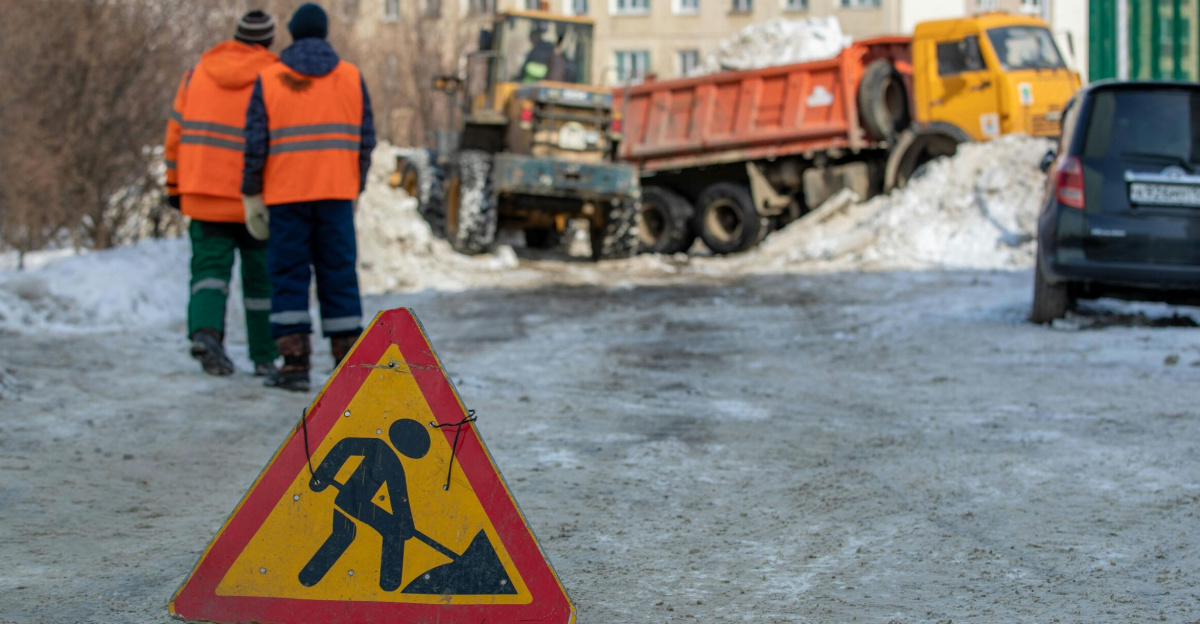 Winter street construction with workers and vehicles in a snowy city setting.