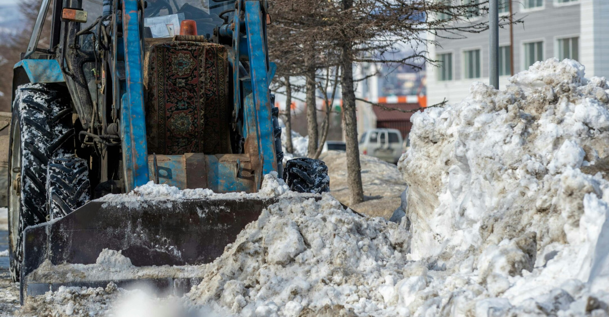A blue tractor plowing snow in an urban area during winter, ensuring road clearance.