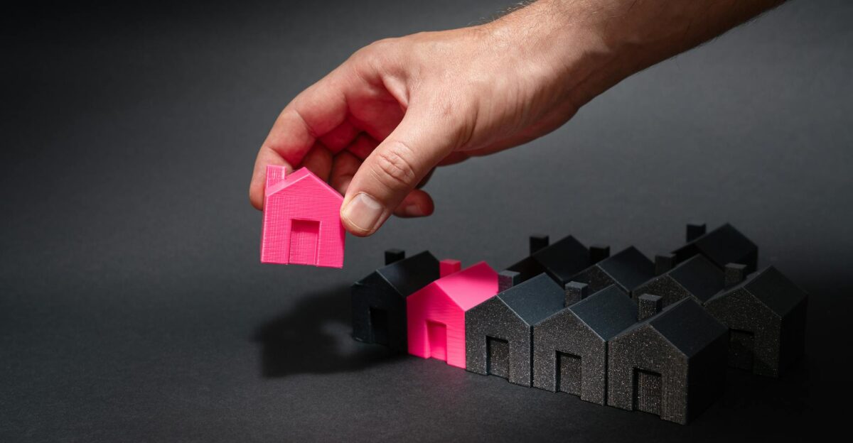 A hand selects a pink mini house among black models symbolizing unique choice