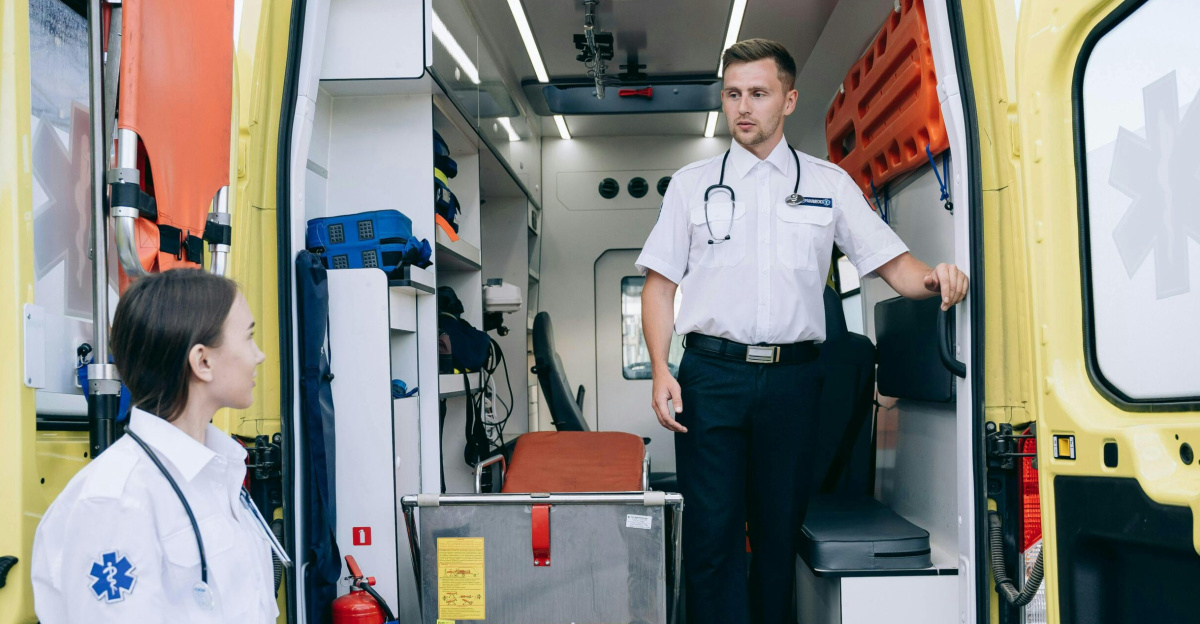 Two paramedics in uniforms and stethoscopes preparing ambulance for upcoming medical emergencies.