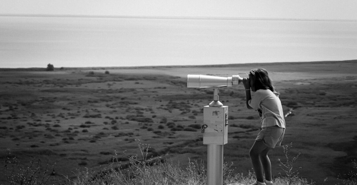 A girl looks through a telescope at the coastal landscape of Enisala Romania