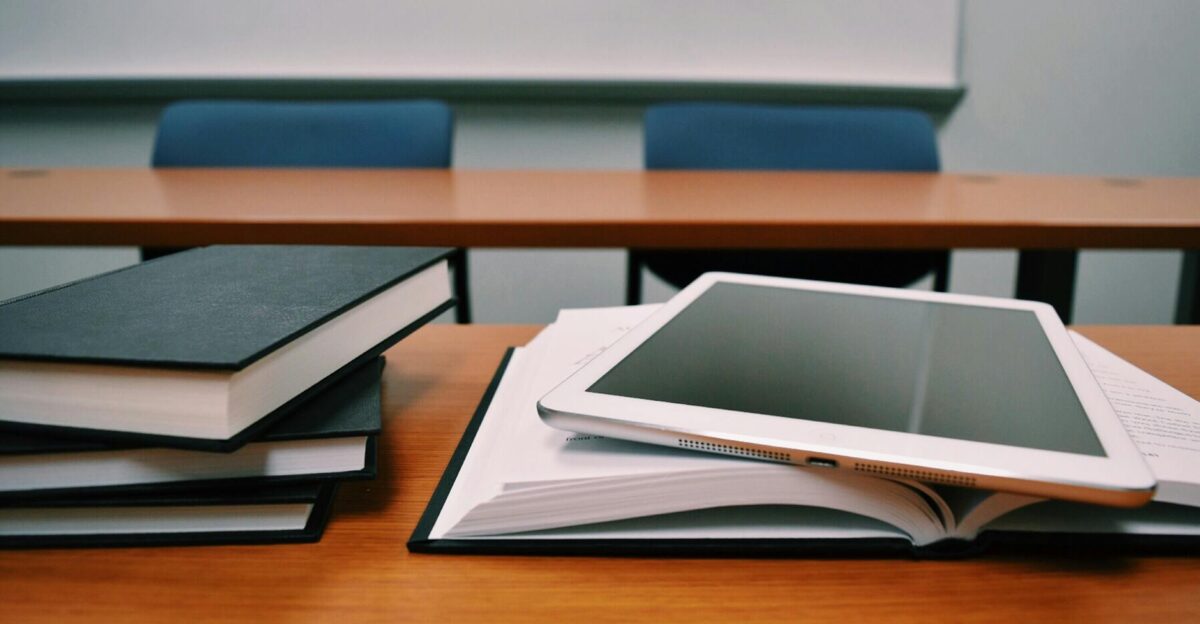 Books and a tablet on a desk in a classroom depicting modern education