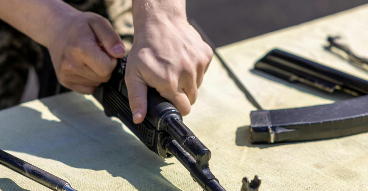 Close-up of a person assembling a rifle on an outdoor table during the day.