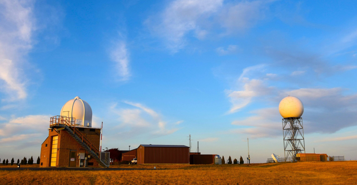 Weather radar station set in a field with a clear blue sky and scattered clouds, showcasing meteorological technology.