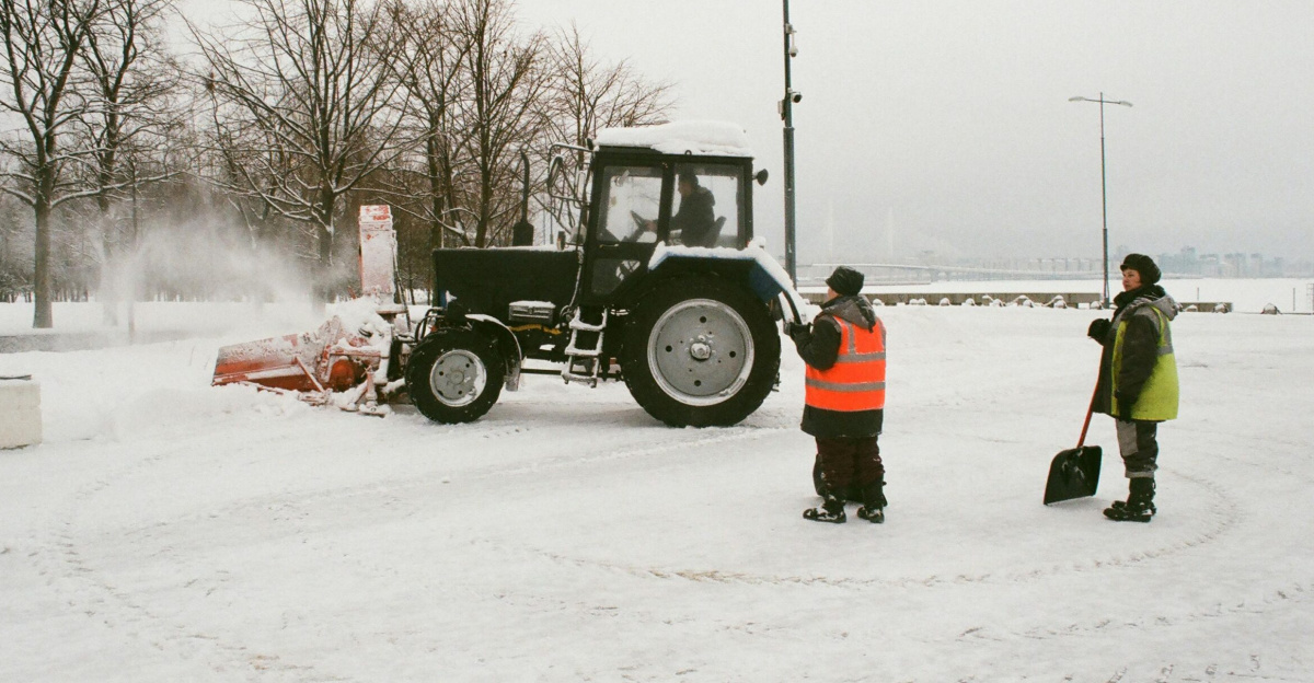 Workers using a tractor to clear snow on a winter street. Image of a snowy scene with road maintenance.