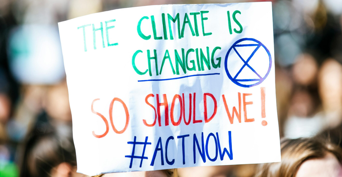 Crowd gathering for climate change protest, holding activist sign.