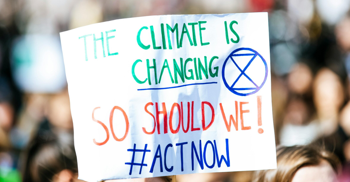 Crowd gathering for climate change protest, holding activist sign.