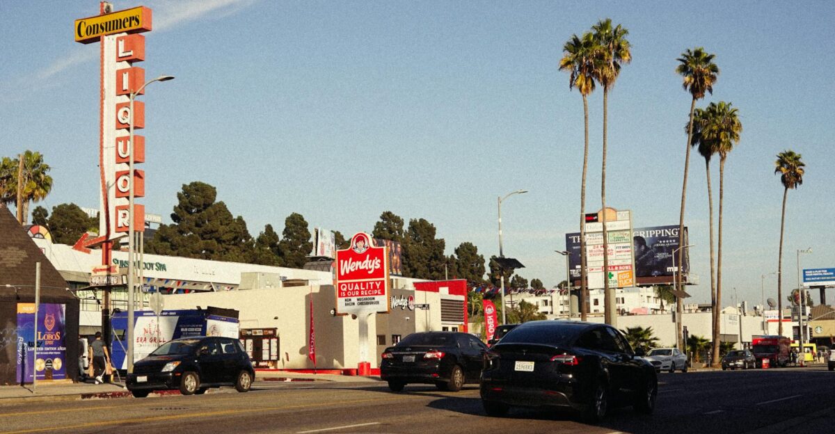 City street with cars palm trees and various signs under a clear sky