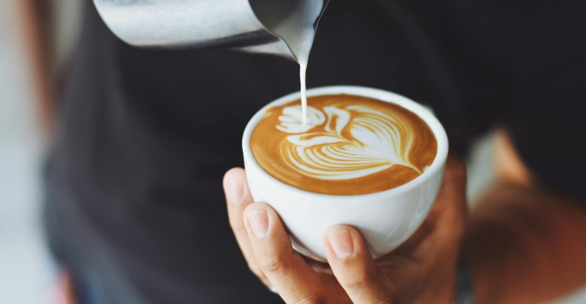 Close-up of a barista pouring milk to create latte art in a coffee cup