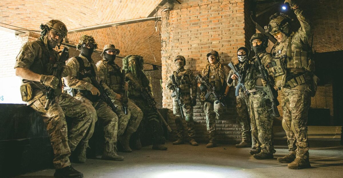 Soldiers in tactical gear gather in a brick underground tunnel with dim lighting