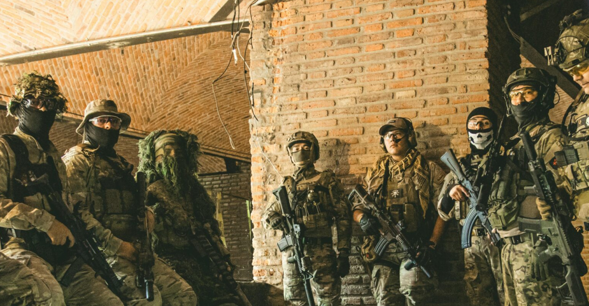 Soldiers in tactical gear gather in a brick underground tunnel with dim lighting.
