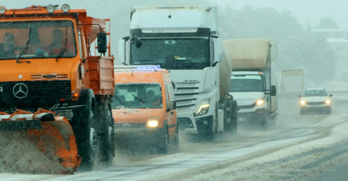 A snow plow leads a line of vehicles on a snowy highway, ensuring safe travel.