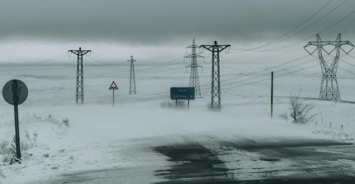 A winter road through snowy landscape with power lines and fog, evoking solitude.