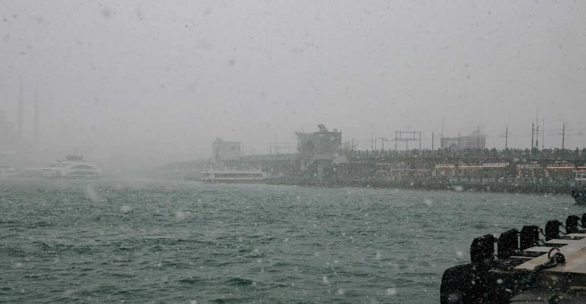 A snowy day at a waterfront with boats and cityscape in the background evoking a serene winter atmosphere