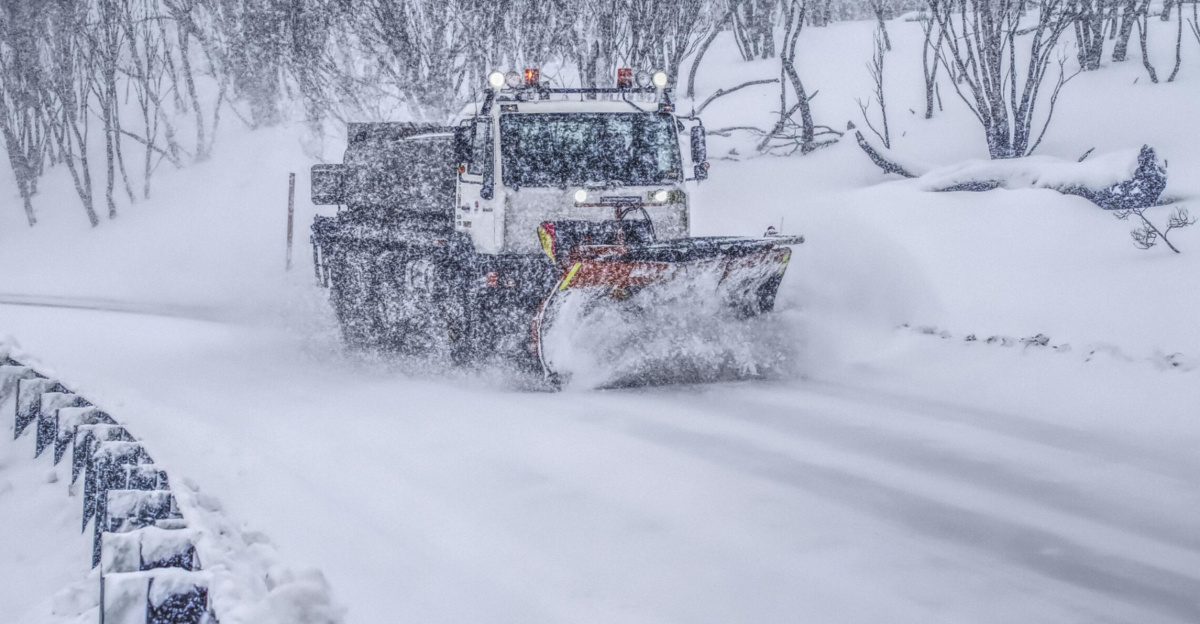 Heavy snowplow clearing a snow-covered road on a snowy winter day.
