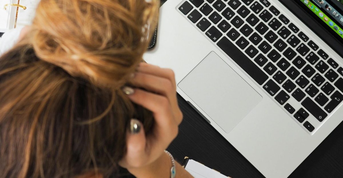 Overhead view of a stressed woman working at a desk with a laptop, phone, and notebooks.
