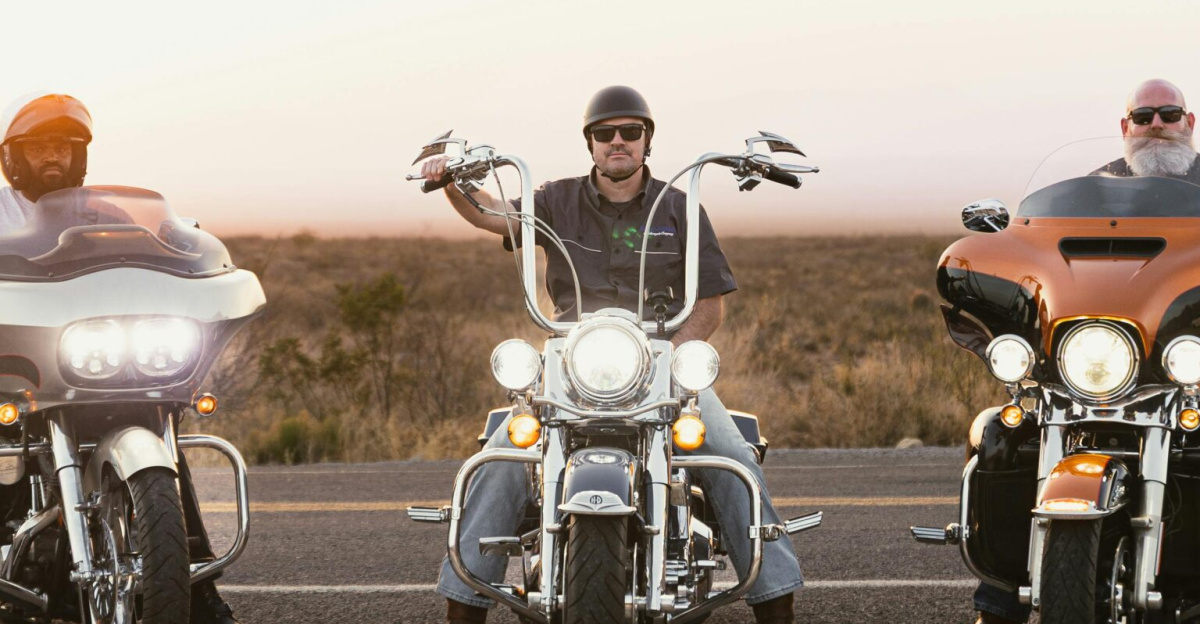 Three bikers on motorcycles riding on a scenic road during sunset in New Mexico.
