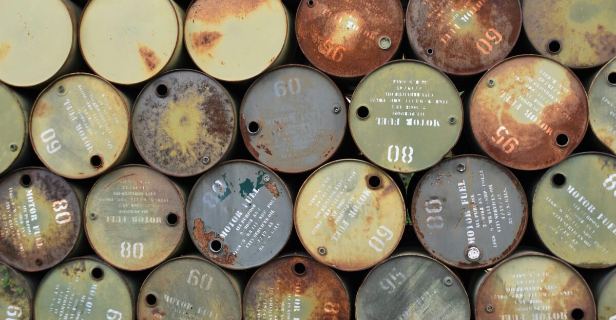 Pile of old rusty oil barrels stacked outdoors with visible labels and numbers