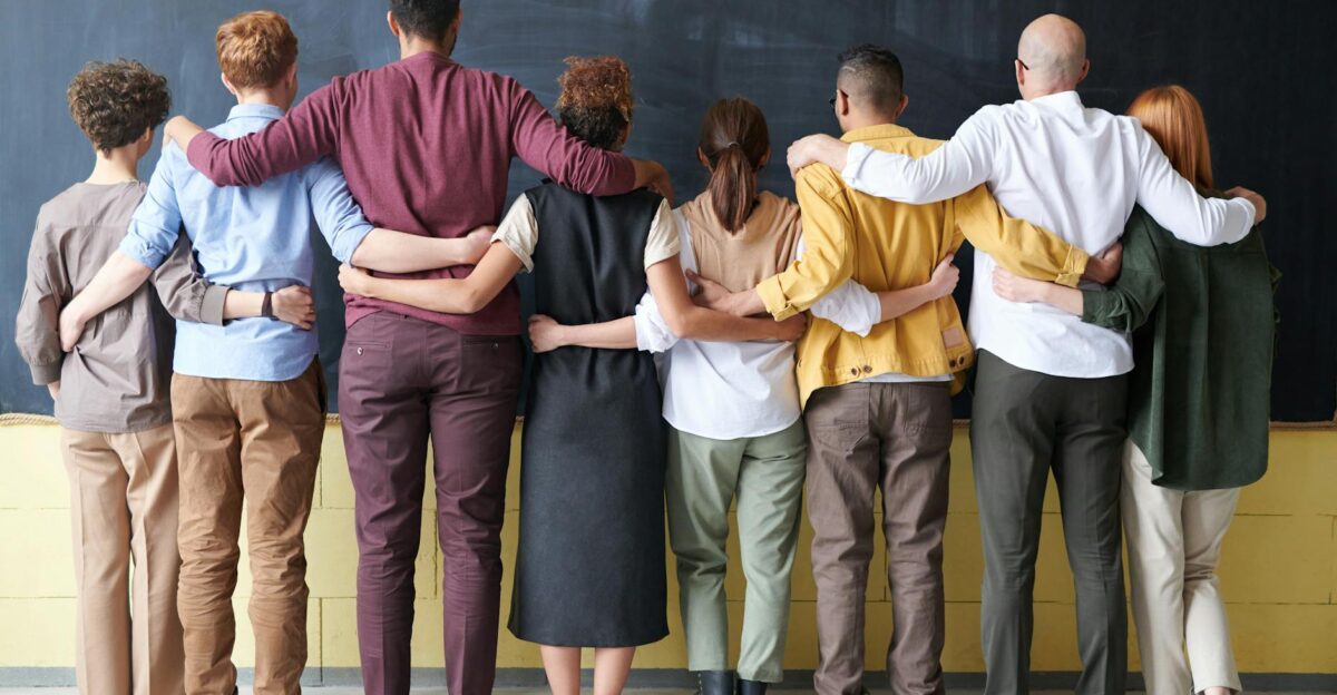 A diverse group of adults in casual outfits hugging in front of a chalkboard symbolizing teamwork