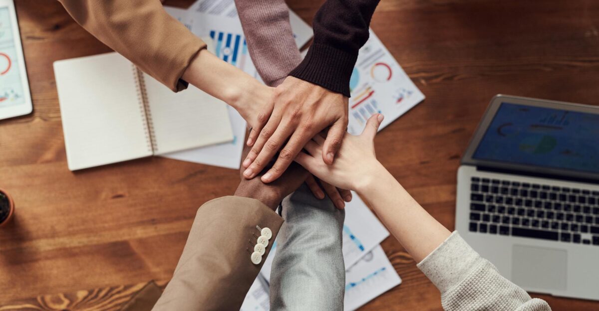 Diverse professionals unite for teamwork around a wooden table with laptops and documents