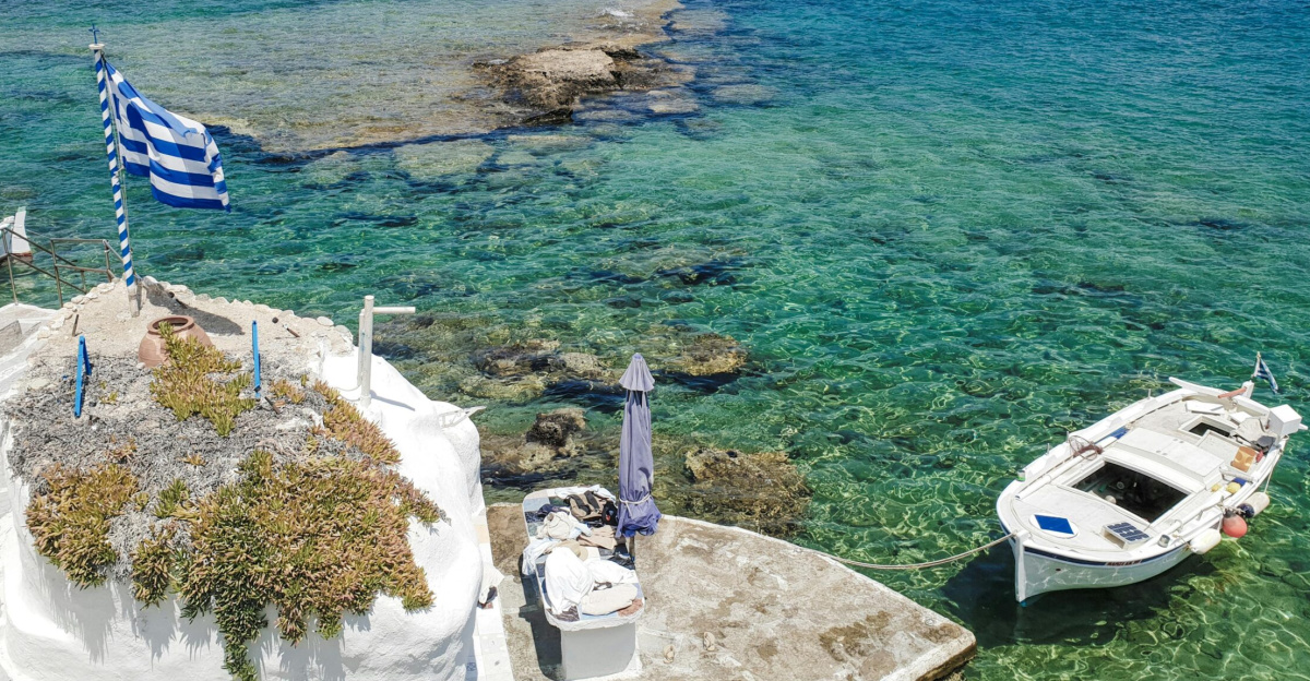Stunning view of a Greek island with clear waters, boats, and traditional architecture.