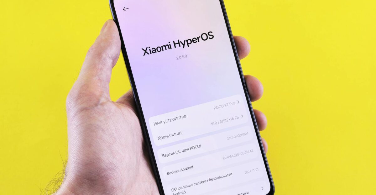 Close-up of a smartphone displaying Xiaomi HyperOS interface held by a hand against a bright yellow background