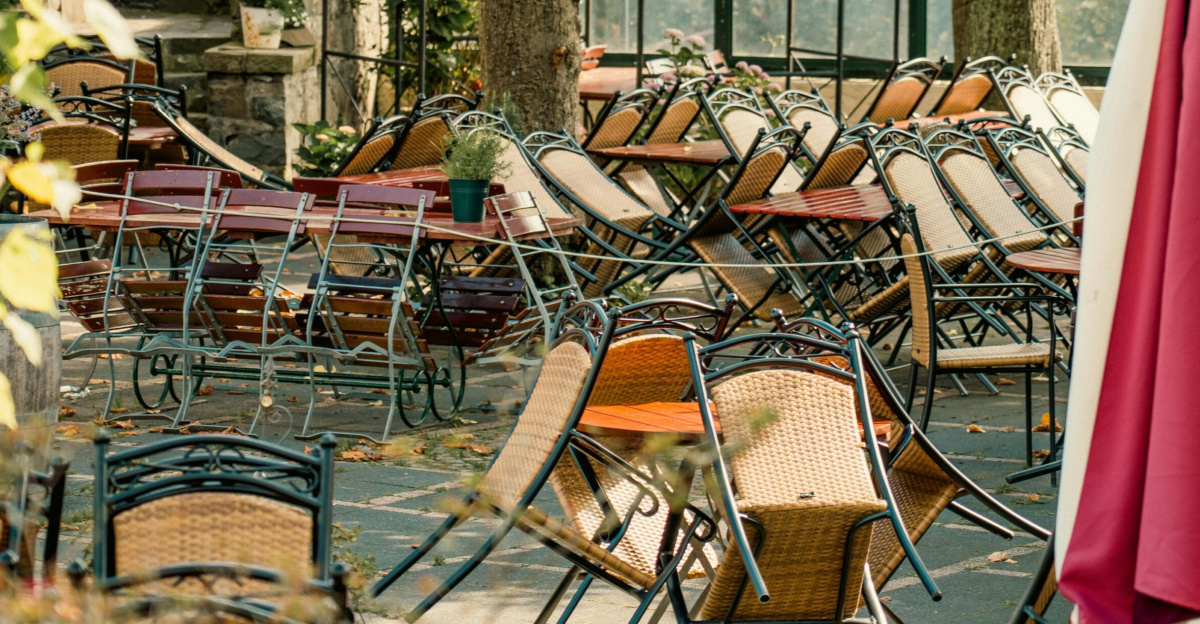 An empty outdoor cafe with stacked chairs and tables in a serene fall setting, indicating closure or off-season.