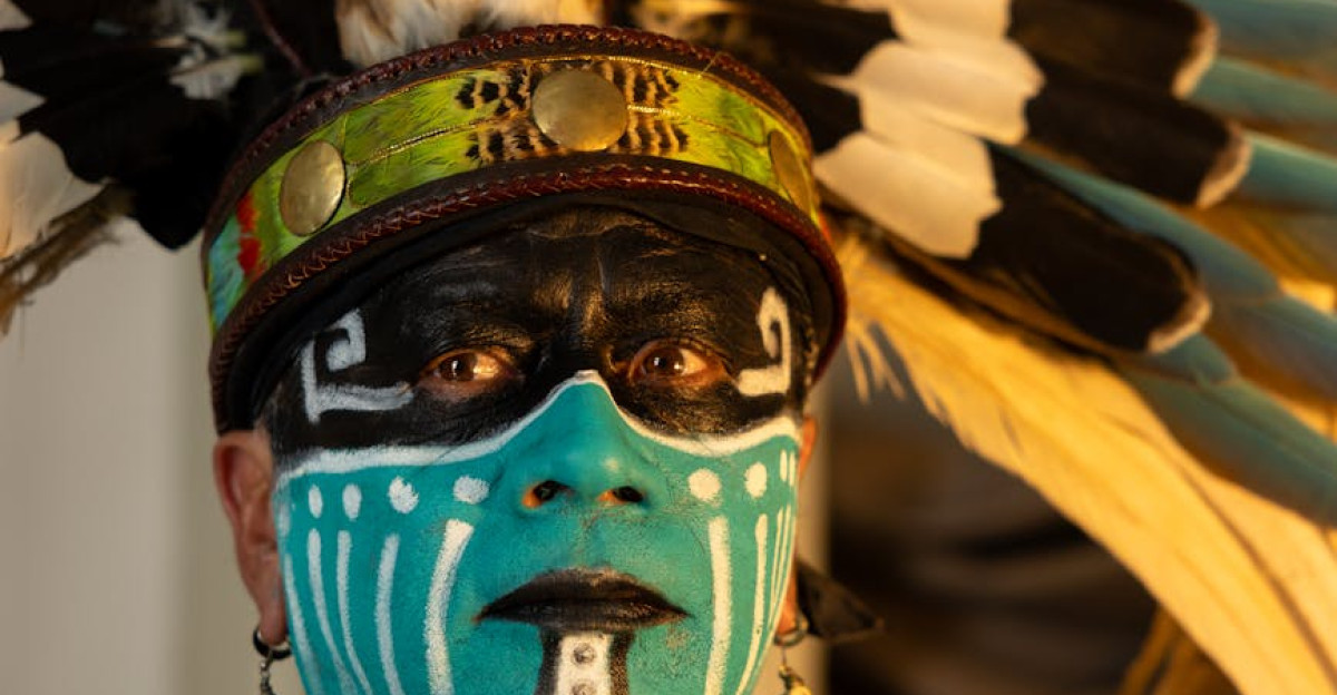 Portrait of an adult in traditional indigenous attire with elaborate feathered headdress and face paint