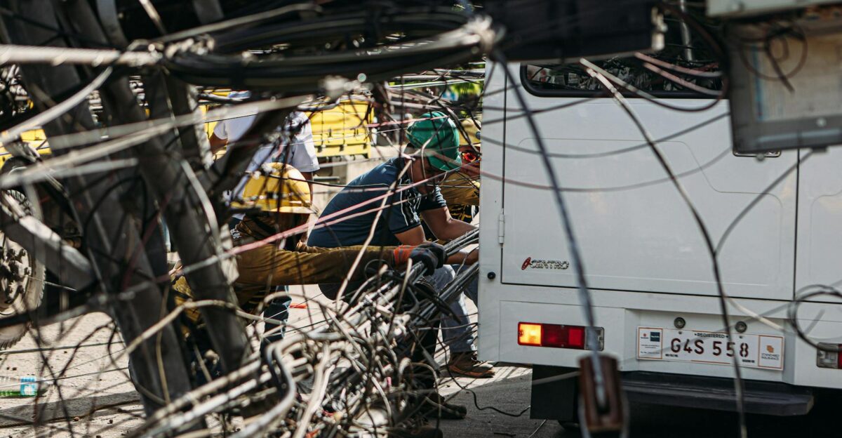 Technicians working on tangled overhead wires next to a vehicle on a sunny day