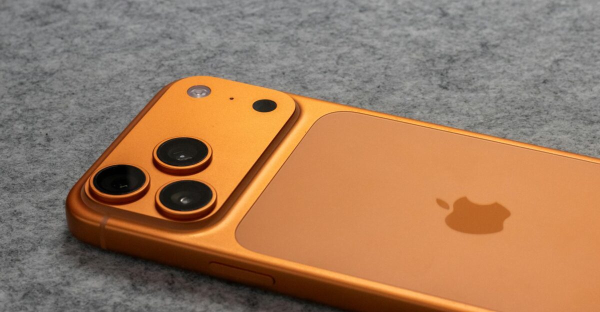 Orange smartphone with dual cameras placed on a soft gray fabric surface