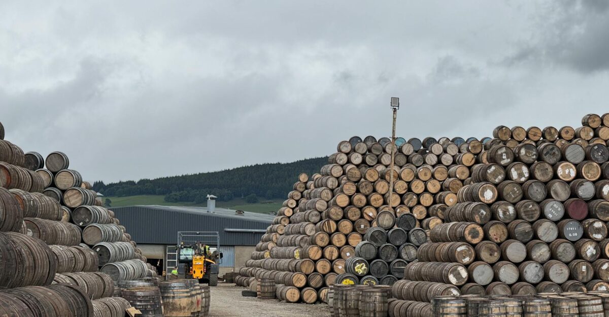 Stacks of whiskey barrels in Dufftown Scotland under a cloudy sky showcasing traditional distillery storage