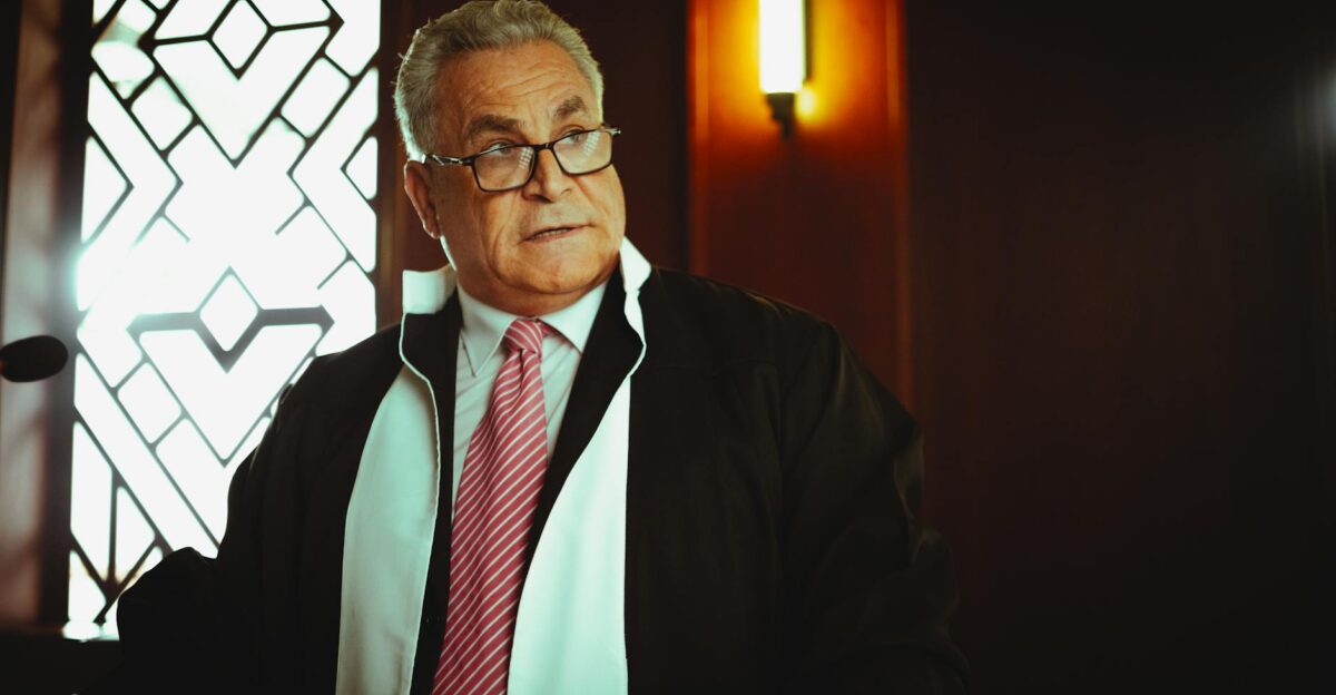 A male judge in a courtroom in Baghdad wearing a robe and tie in a contemplative pose