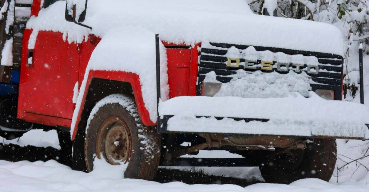A red truck blanketed by snow in a serene winter forest setting, showcasing nature's beauty.
