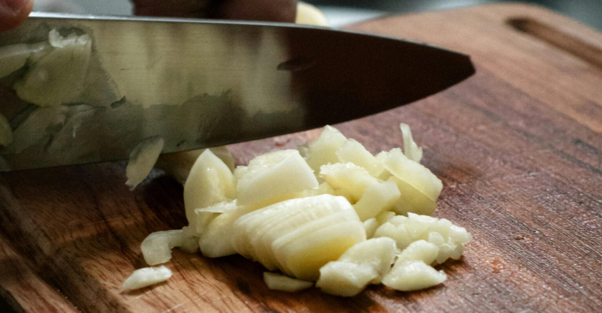 Close-up of garlic being finely chopped on a wooden cutting board in a kitchen setting.