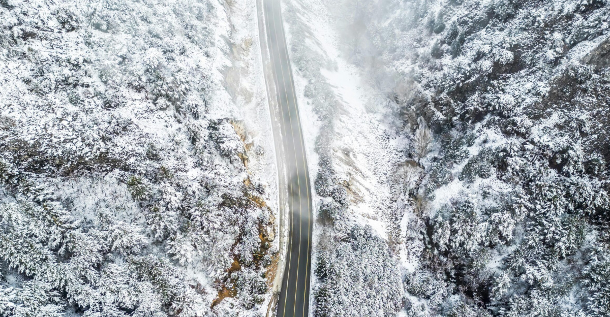 Aerial view of a winding road through a snowy forest, showcasing winter's beauty.