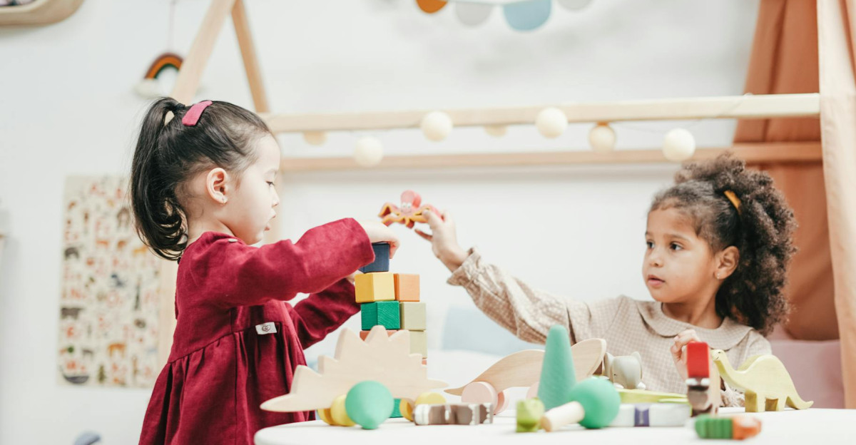 Two young girls enjoying playtime with wooden toys indoors in a warm colorful playroom