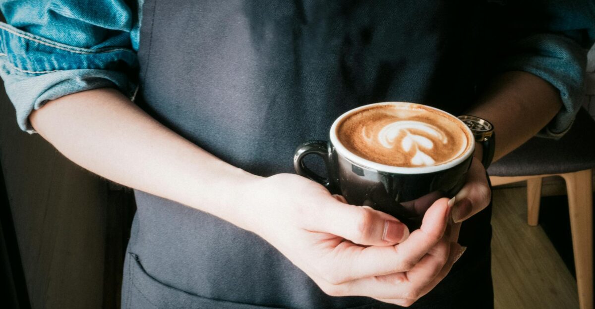 A barista holds a coffee cup with beautiful latte art in a cozy caf setting