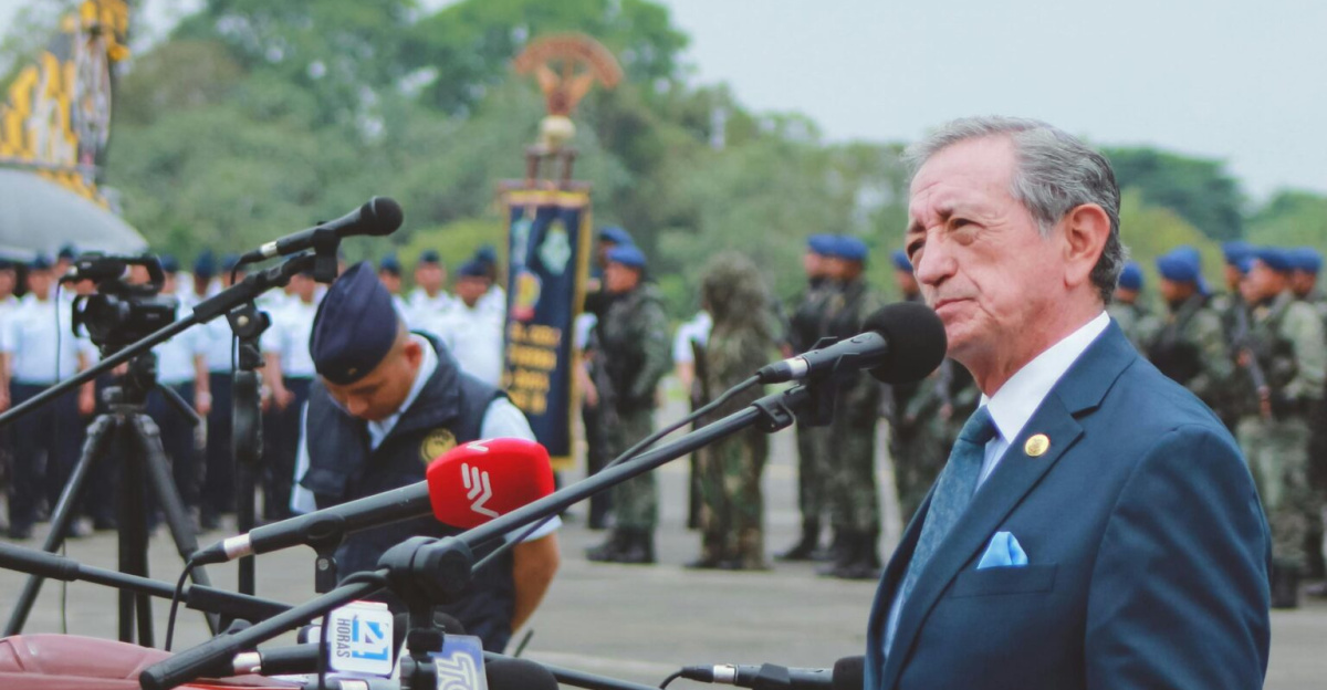 Side view of mature colonel with order standing near microphones on asphalt pavement behind army of soldiers near airplane monument under serene sky during national military holiday and looking away
