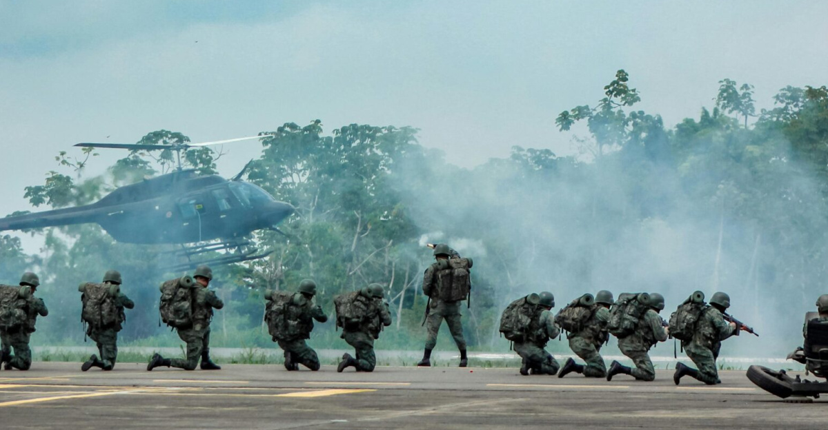 Military personnel in action during a training exercise with helicopter support and weapon artillery outdoors.