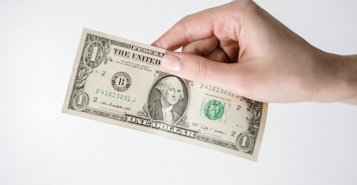 Close-up of a Caucasian hand holding a US one dollar bill against a white background
