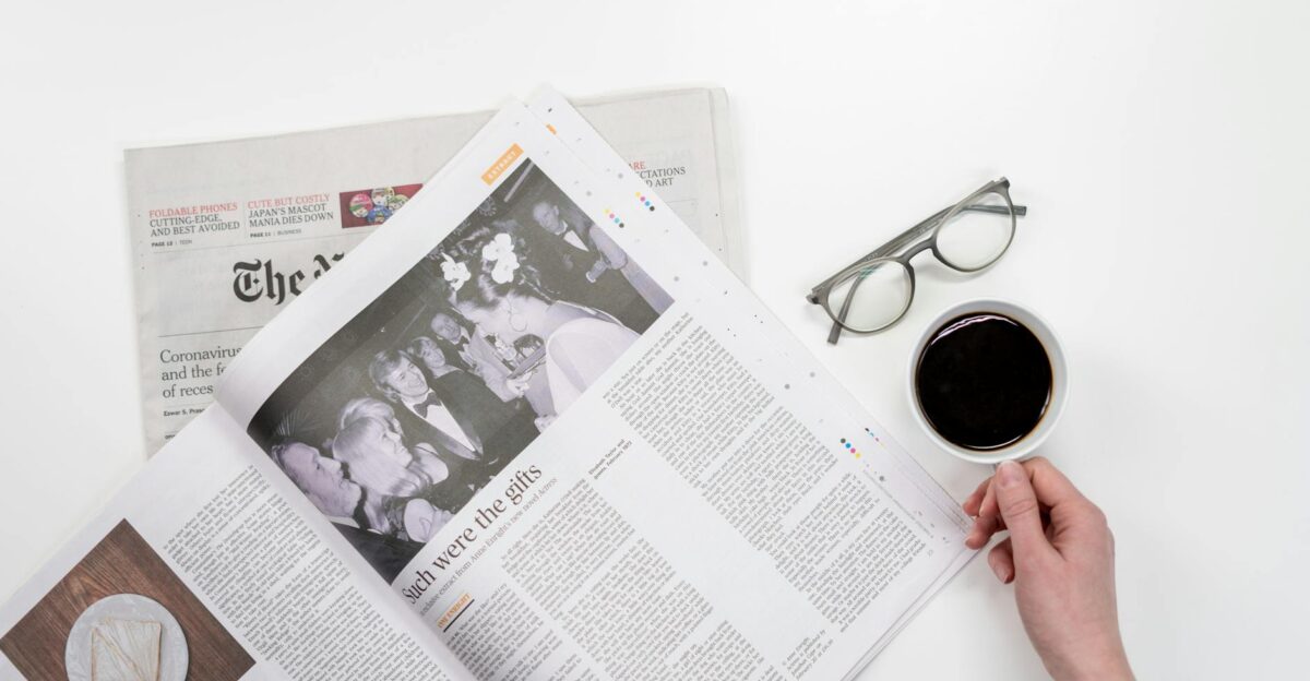 Overhead view of newspaper reading with coffee and glasses on a white table