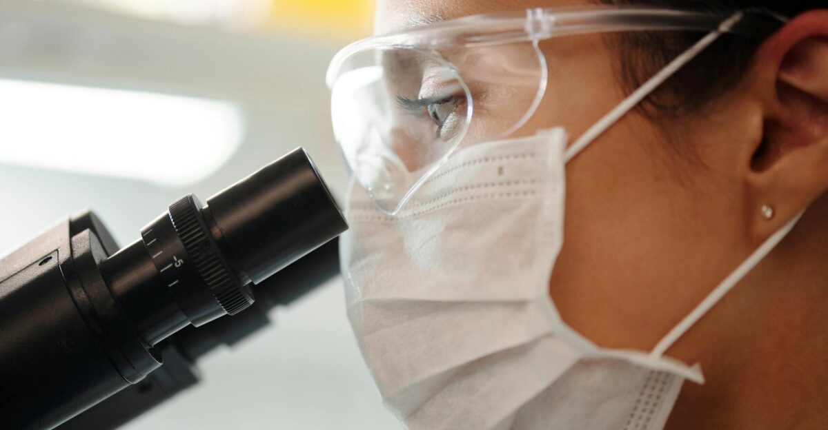 Close-up of a researcher with safety gear using a microscope in a lab