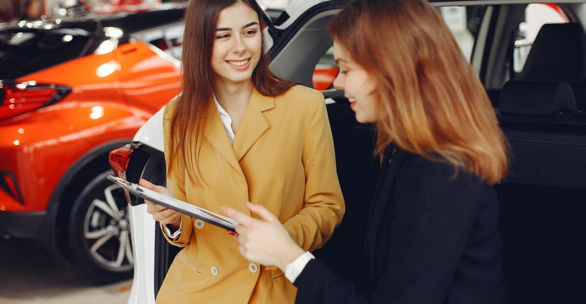 Two women engaged in a conversation about purchasing a car in a dealership showroom